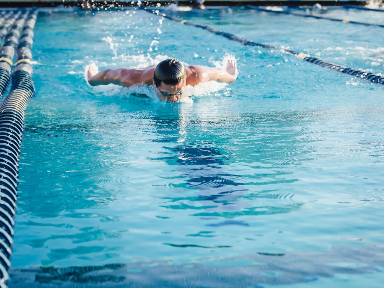 Mastering the First Impression: Your intriguing post title goes here Athletic swimmer performing butterfly stroke in clear blue pool, showcasing skill and technique.